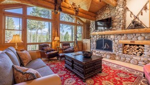 Un intérieur chaleureux de chalet en bois avec une cheminée en pierre, de grandes fenêtres et un décor rustique.