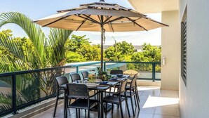 Ein Balkon mit Esstisch und Stühlen, beschattet durch einen Sonnenschirm.