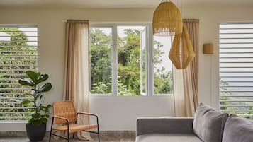 A room with a large window, a wicker chair, a grey sofa, and a hanging light fixture.