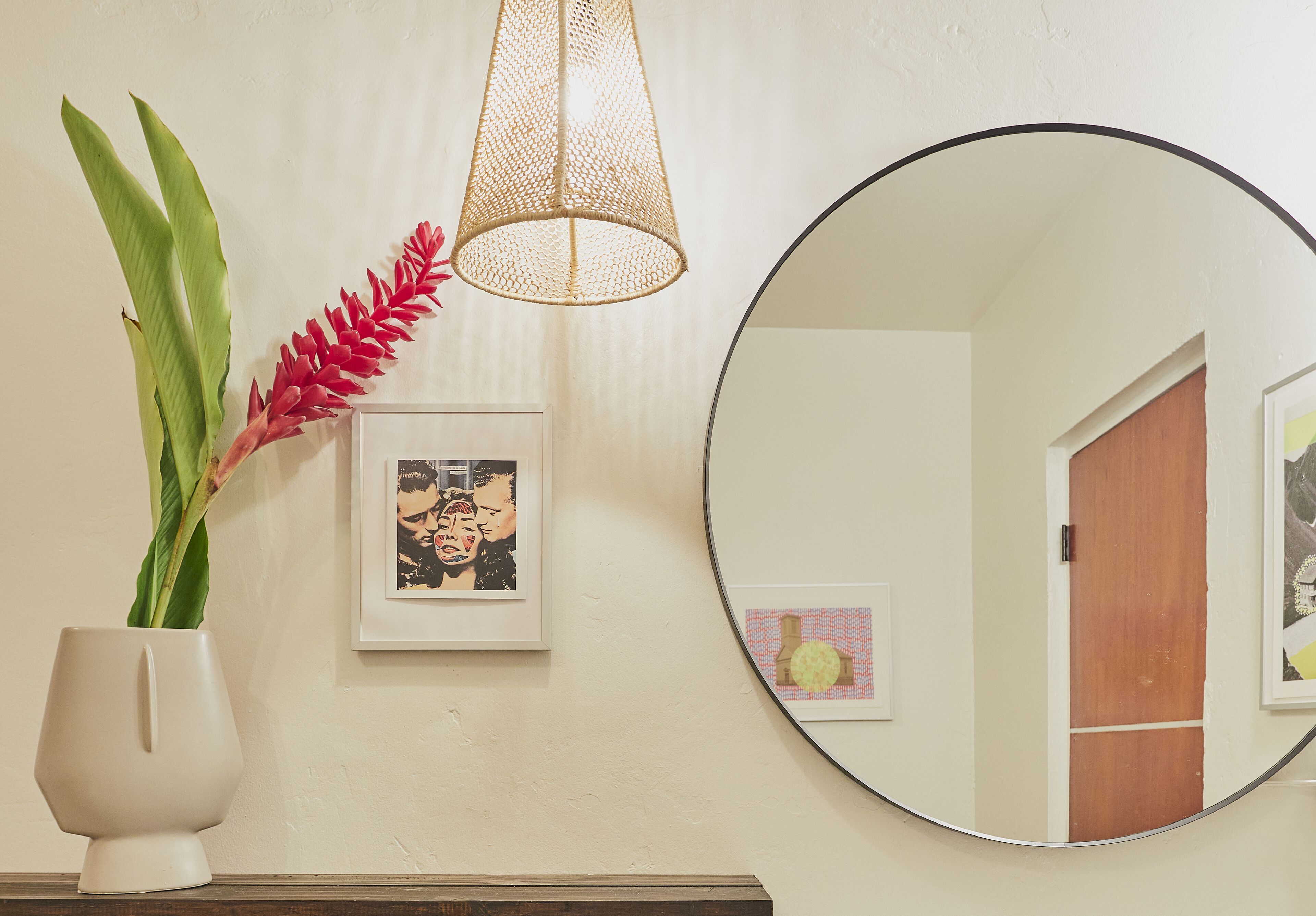 A wall with a round mirror, a framed picture, and a potted plant.