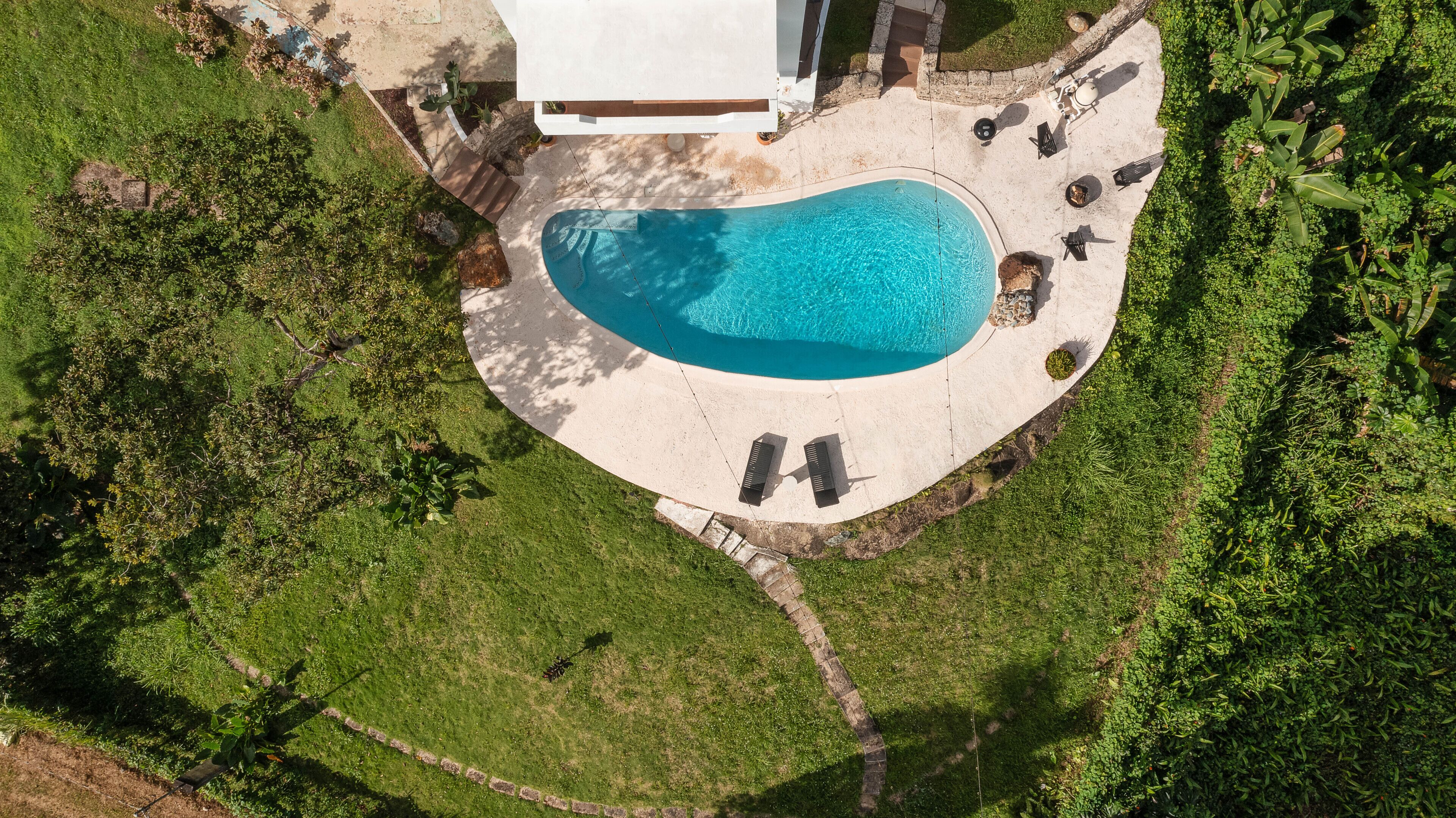 Vista aérea de una piscina rodeada por un patio con sillas de descanso y una pequeña terraza.