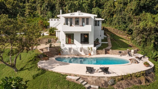 Ein modernes, zweistöckiges Haus mit Swimmingpool, umgeben von üppiger Vegetation.