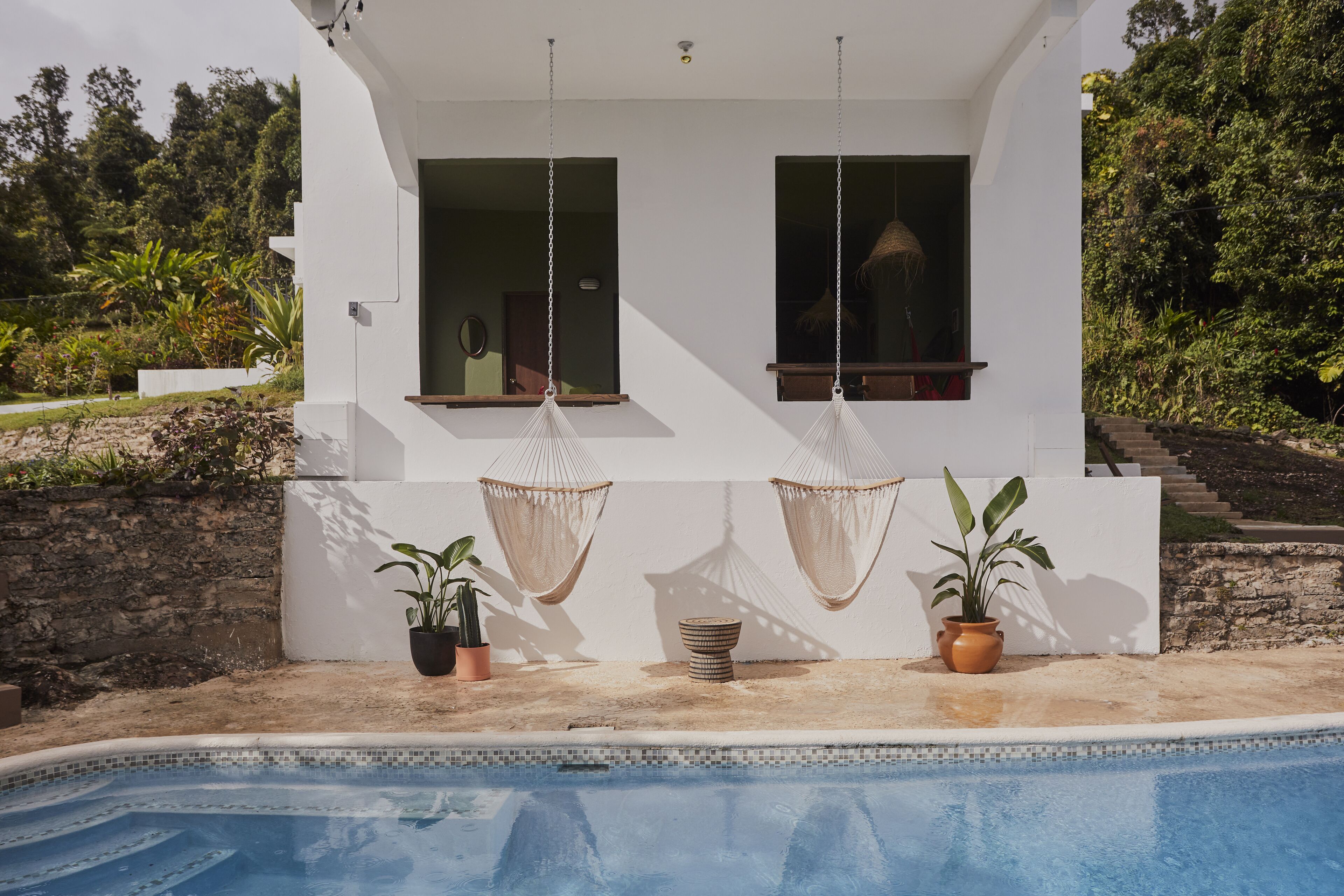 Una casa moderna con piscina, dos columpios y plantas en macetas.