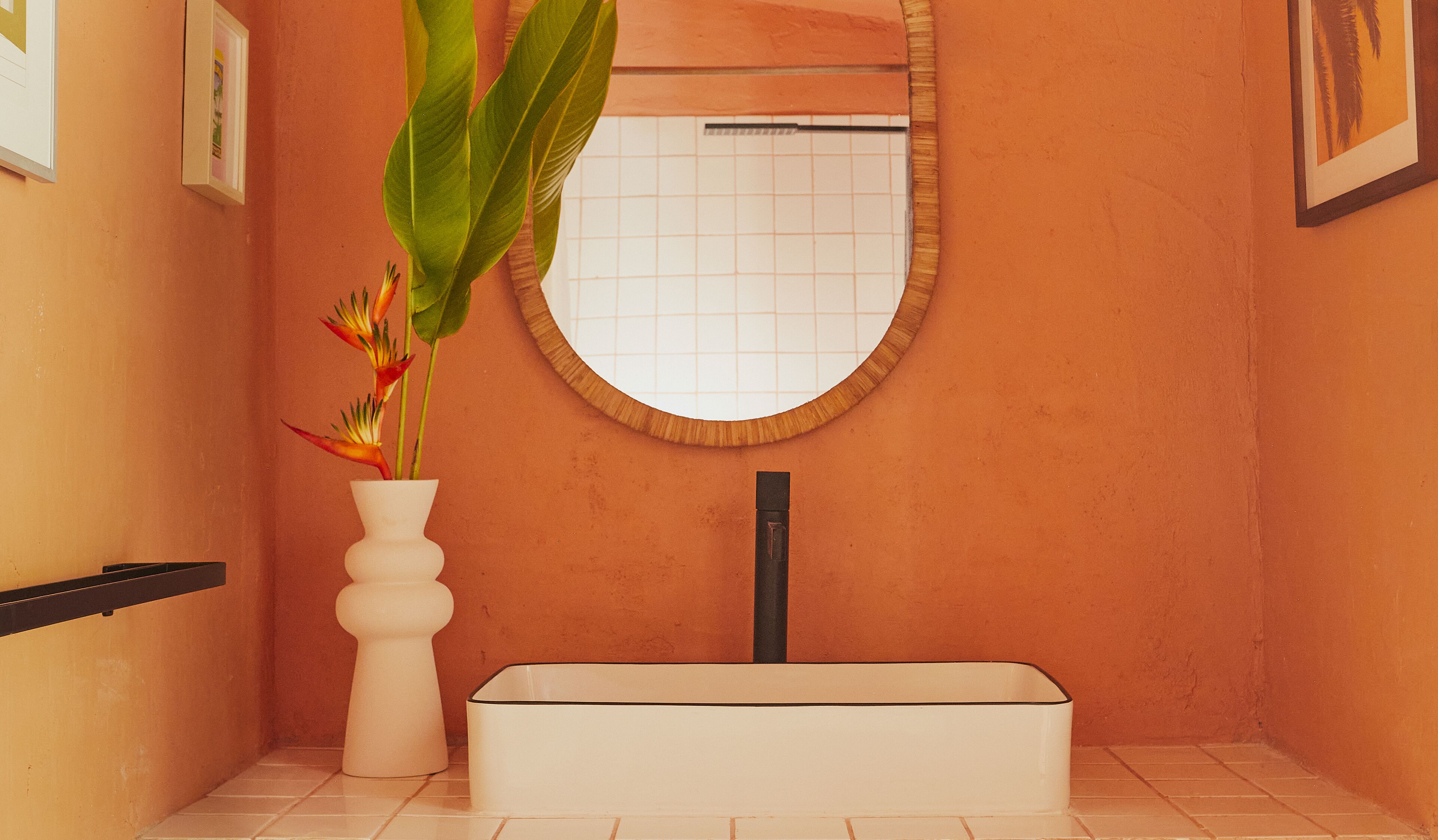 A bathroom with a white bathtub, a round mirror, and a white vase with a plant.