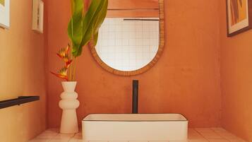 A bathroom with a white bathtub, a round mirror, and a white vase with a plant.