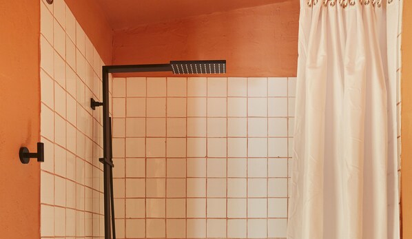 Un baño con zona de ducha azulejada, una cortina blanca y un cabezal de ducha negro.