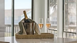 Eine Champagnerflasche in einem Metallkübel auf einer gewebten Matte, daneben zwei Champagnergläser.