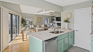 Eine moderne Küche mit einer großen Kochinsel, ein Essbereich mit Tisch und Stühlen sowie ein Wohnzimmer mit Sofa und Dekorationselementen.