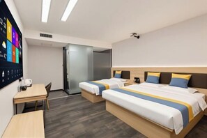 Habitación de hotel con dos camas, un escritorio, un televisor de pantalla plana y una puerta que da a un baño.