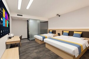 A hotel room with two beds, a desk, a flat-screen TV, and a door leading to a bathroom.