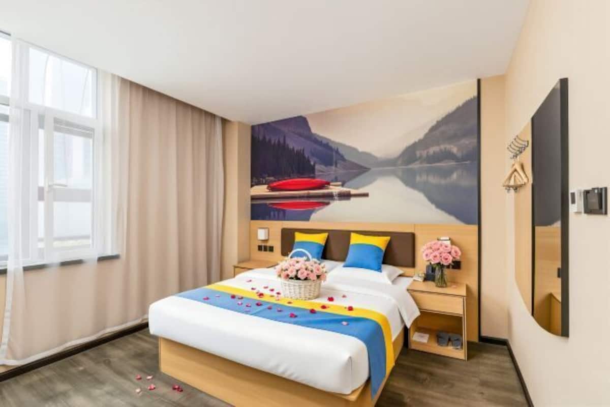 A hotel room with a large bed, a nightstand, a wall-mounted mirror, and a window with curtains.