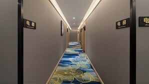 A hotel hallway with a patterned carpet, wall-mounted signs, and a ceiling light.
