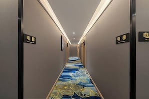 A hotel hallway with a patterned carpet, wall-mounted signs, and a ceiling light.