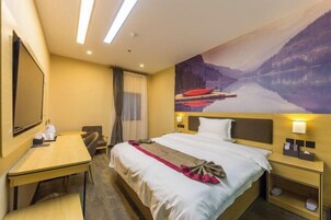 Una habitación de hotel con cama, escritorio, silla, televisor y un cuadro de un paisaje montañoso.