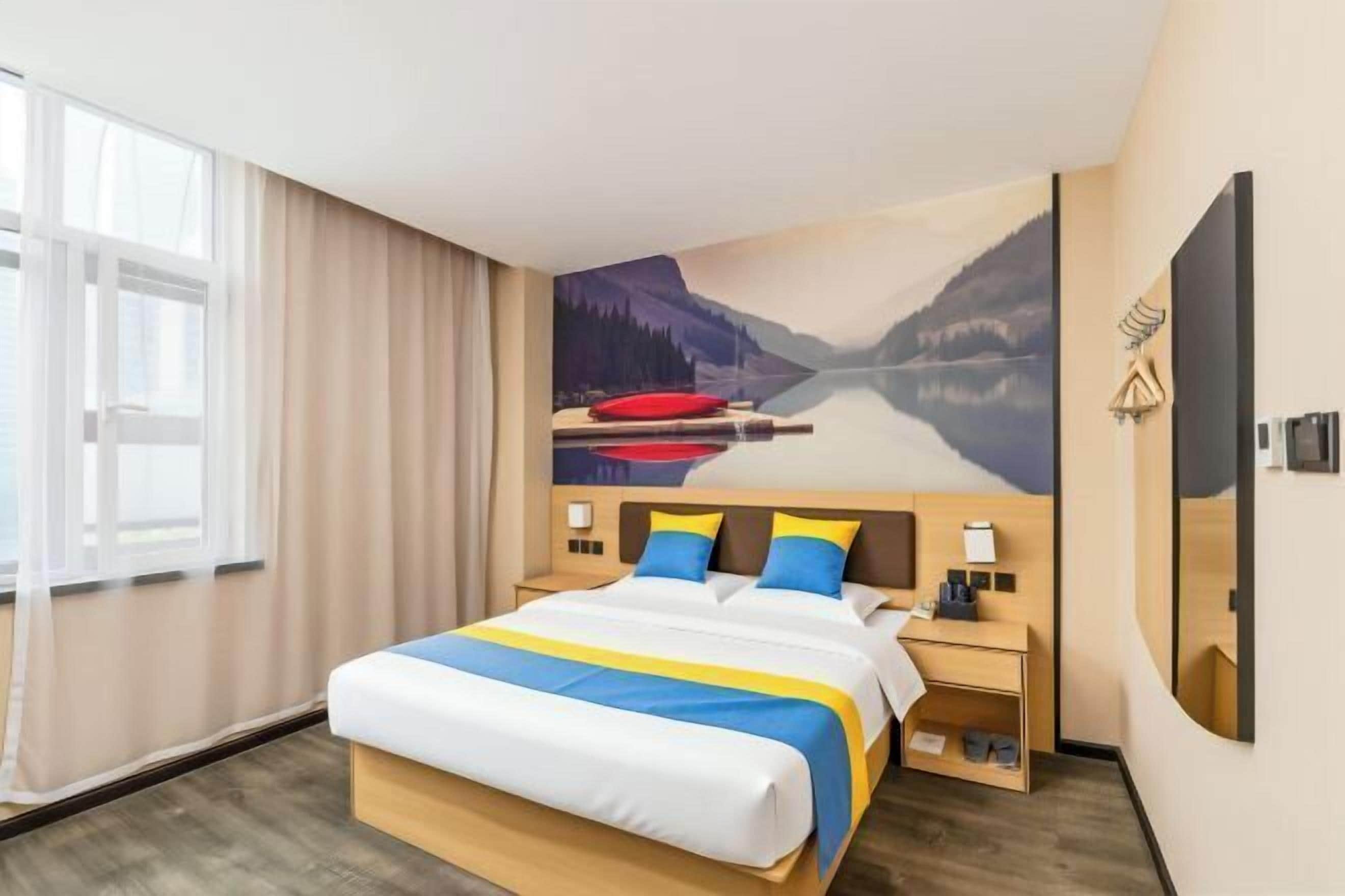 Una habitación de hotel con una cama, una mesita de noche, una lámpara de pared y un ventanal con cortinas.