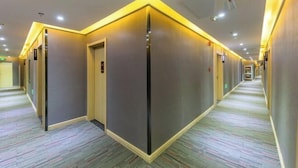 A hotel corridor with a modern design, featuring a carpeted floor and a series of doors along the walls.