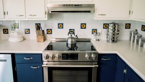 Eine Küche mit weißen Schränken, einem Herd, einem Backofen und einer Kaffeemaschine.