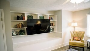 Ein Wohnzimmer mit Flachbildfernseher, der an einer weißen Unterhaltungsecke befestigt ist, umgeben von Regalen mit Büchern und Dekoration.