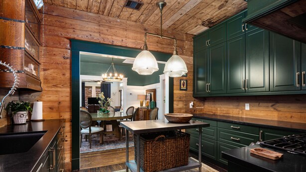 Una cocina con armarios de madera, un comedor con mesa y sillas, y una lámpara colgante.