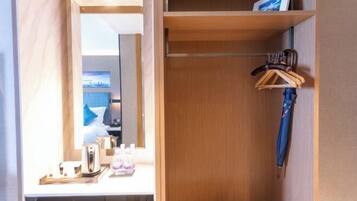 A hotel room with a wooden vanity, a mirror, a small table with a kettle and bottles, and a hanging blue umbrella.
