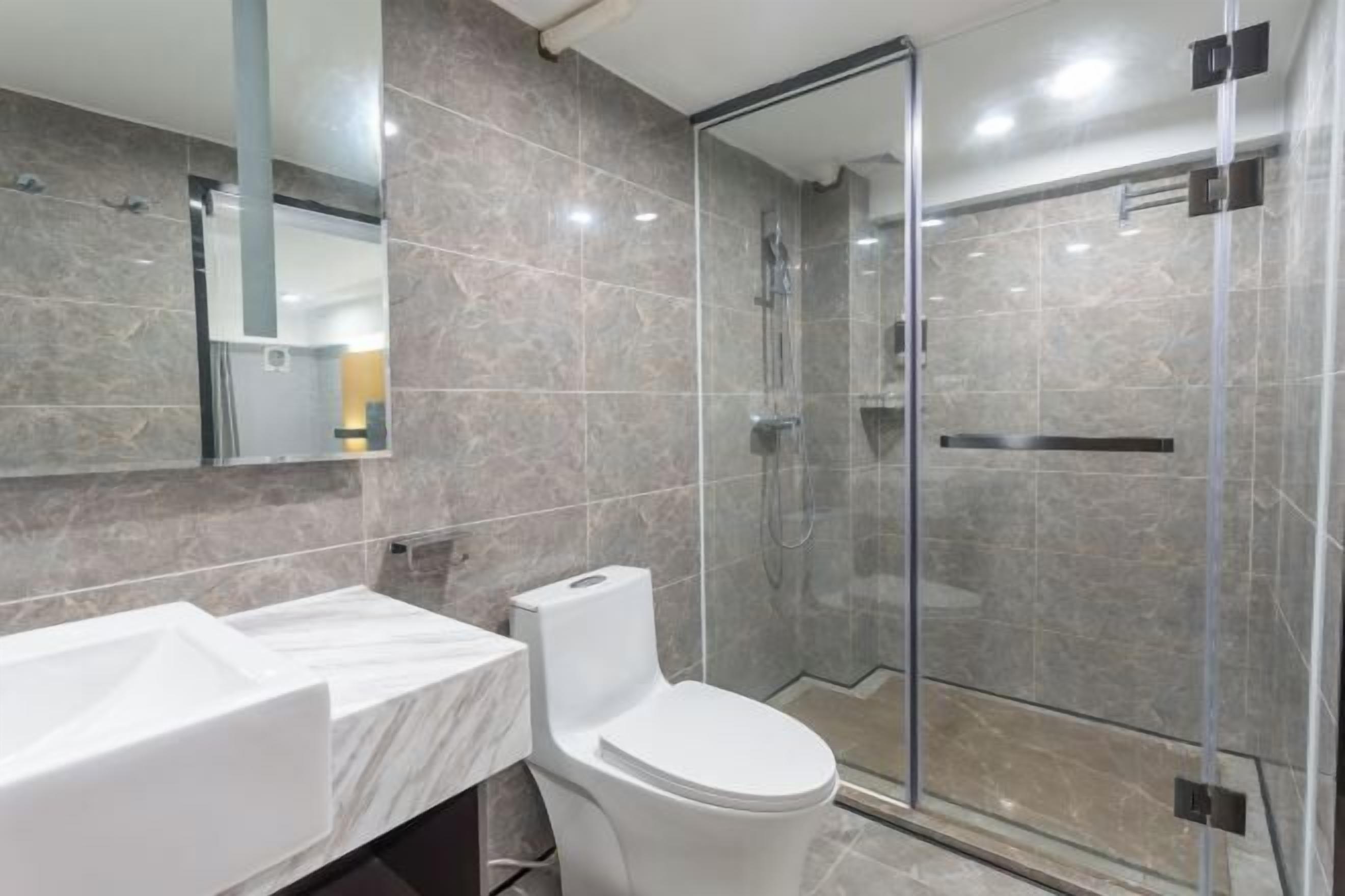 Un baño moderno con tocador de mármol, inodoro y ducha con mampara de vidrio.