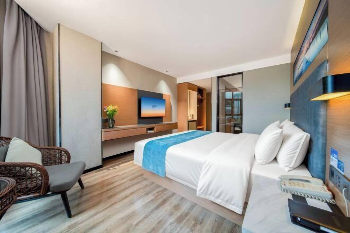 A modern hotel room with a bed, a desk, a chair, a TV, and a bathroom.