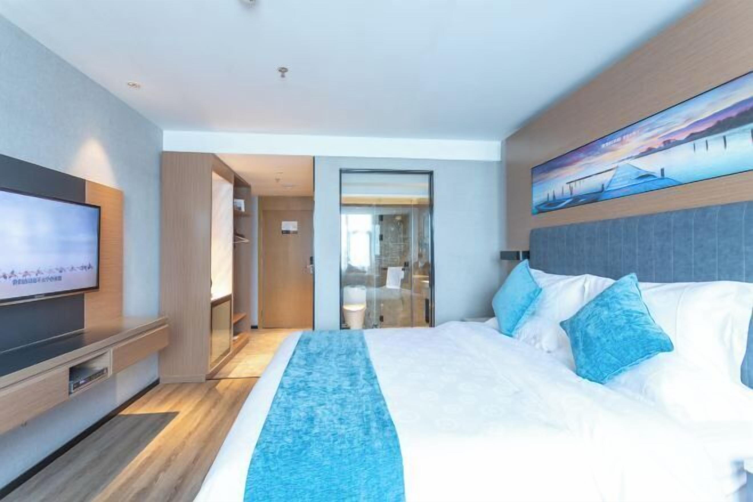 A modern hotel room with a large bed, a flat-screen TV, and a painting above the bed.