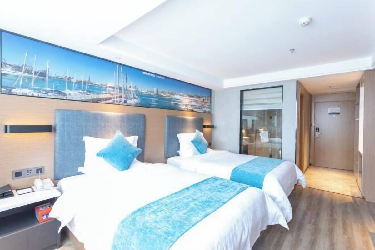 A hotel room with two beds, a large window, and a view of a marina.