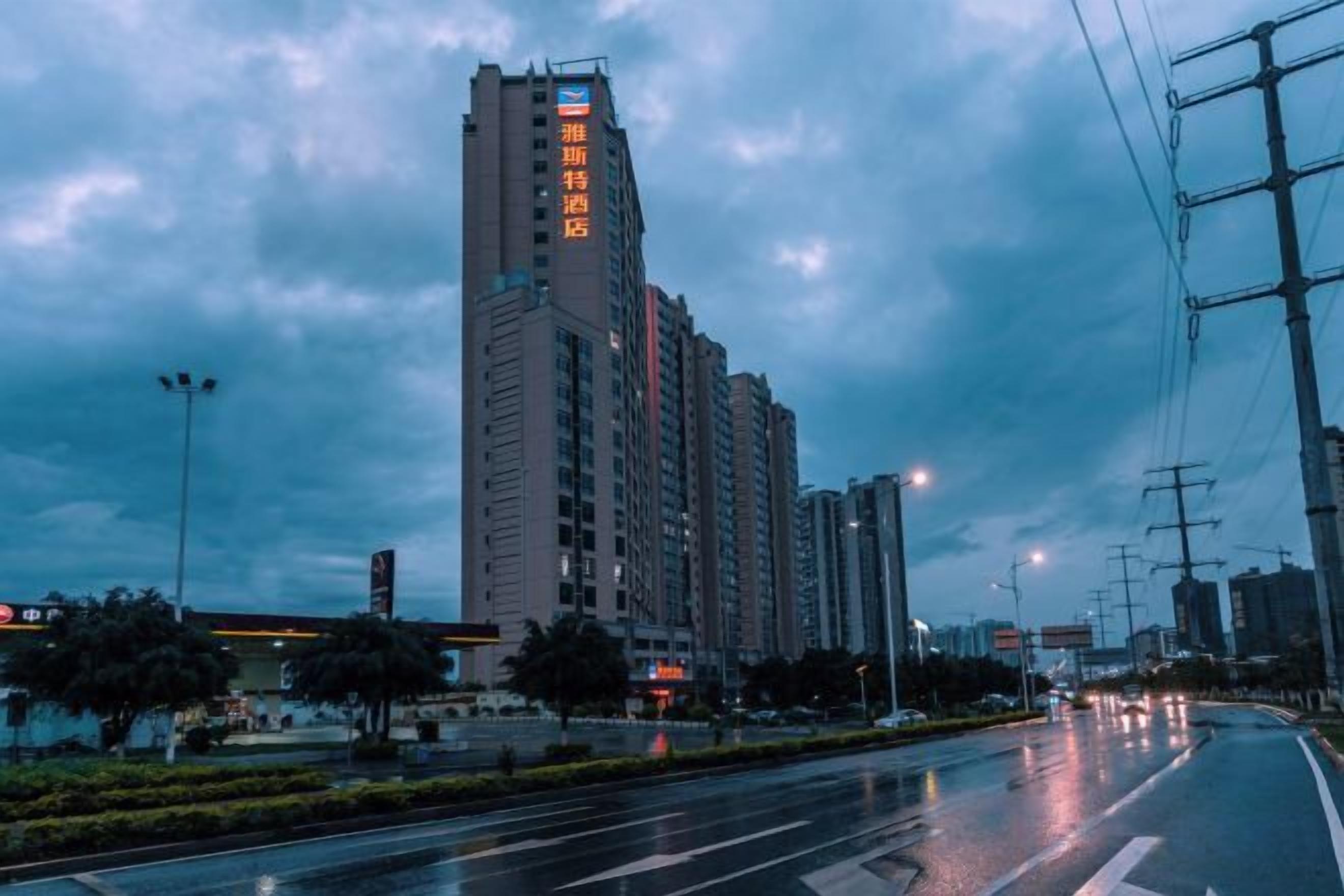 Un immeuble à plusieurs étages, avec une enseigne bien visible sur la façade, une large rue où circulent des véhicules et des lampadaires.
