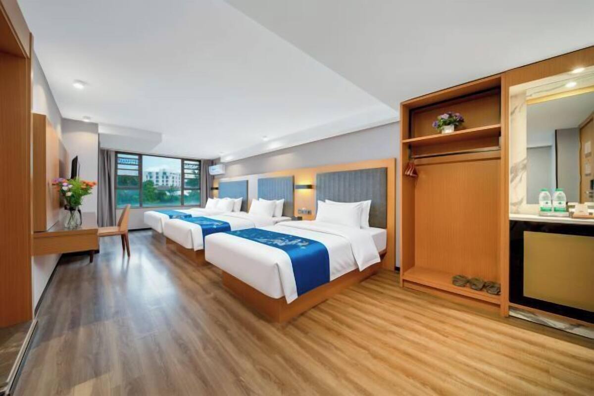 A hotel room with two beds, a desk, a mirror, and a view of the outside.
