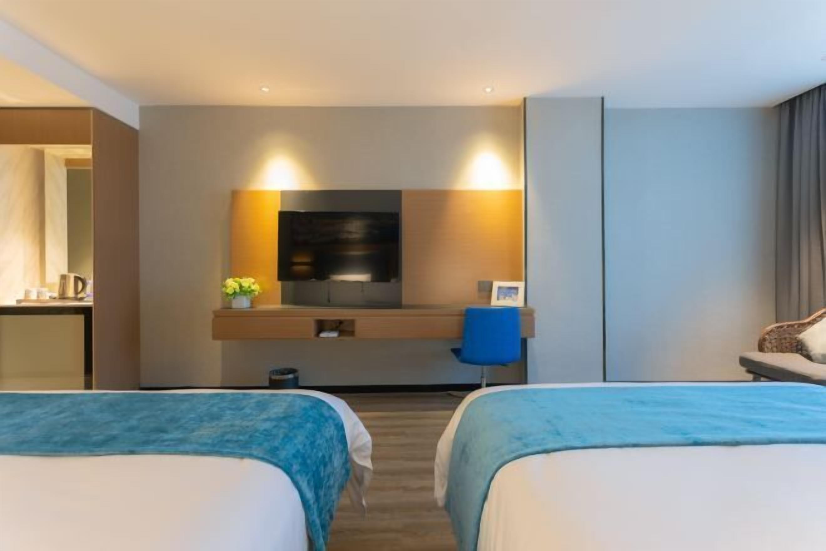 A hotel room with two beds, a desk, a TV, and a bathroom.