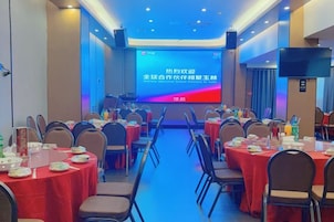 Un salón de conferencias con varias mesas y sillas, una pantalla grande al frente y una alfombra azul.