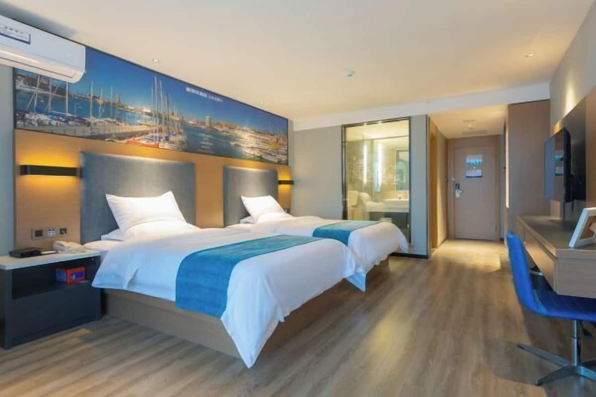 A hotel room with two beds, a desk, and a bathroom visible through an open door.