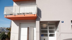 A two-story building with a white facade, a balcony with a glass railing, and a garage door. - Apartment Josip - One Bedroom apartment (Zagreb)