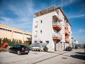 Un immeuble résidentiel à plusieurs étages, doté de balcons, d’un espace de stationnement couvert et d’une aire de jeux en arrière-plan.