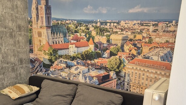 A living room with a sofa, a radiator, and a wall mural of a cityscape. - Apartment Josip - One Bedroom apartment (Zagreb)