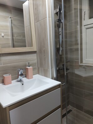 Ein modernes Badezimmer mit einem weißen Waschbecken, zwei rosa Seifenspendern, einem Spiegel und einer Duschkabine aus Glas.