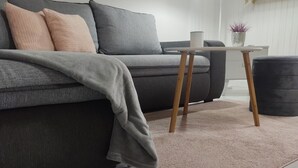 Un salon moderne avec un canapé gris, une petite table d’appoint en bois et un tapis rose.