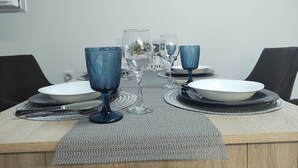 Une table à manger dressée avec de la verrerie bleue, des verres transparents et des assiettes blanches, et une horloge en bois au-dessus.