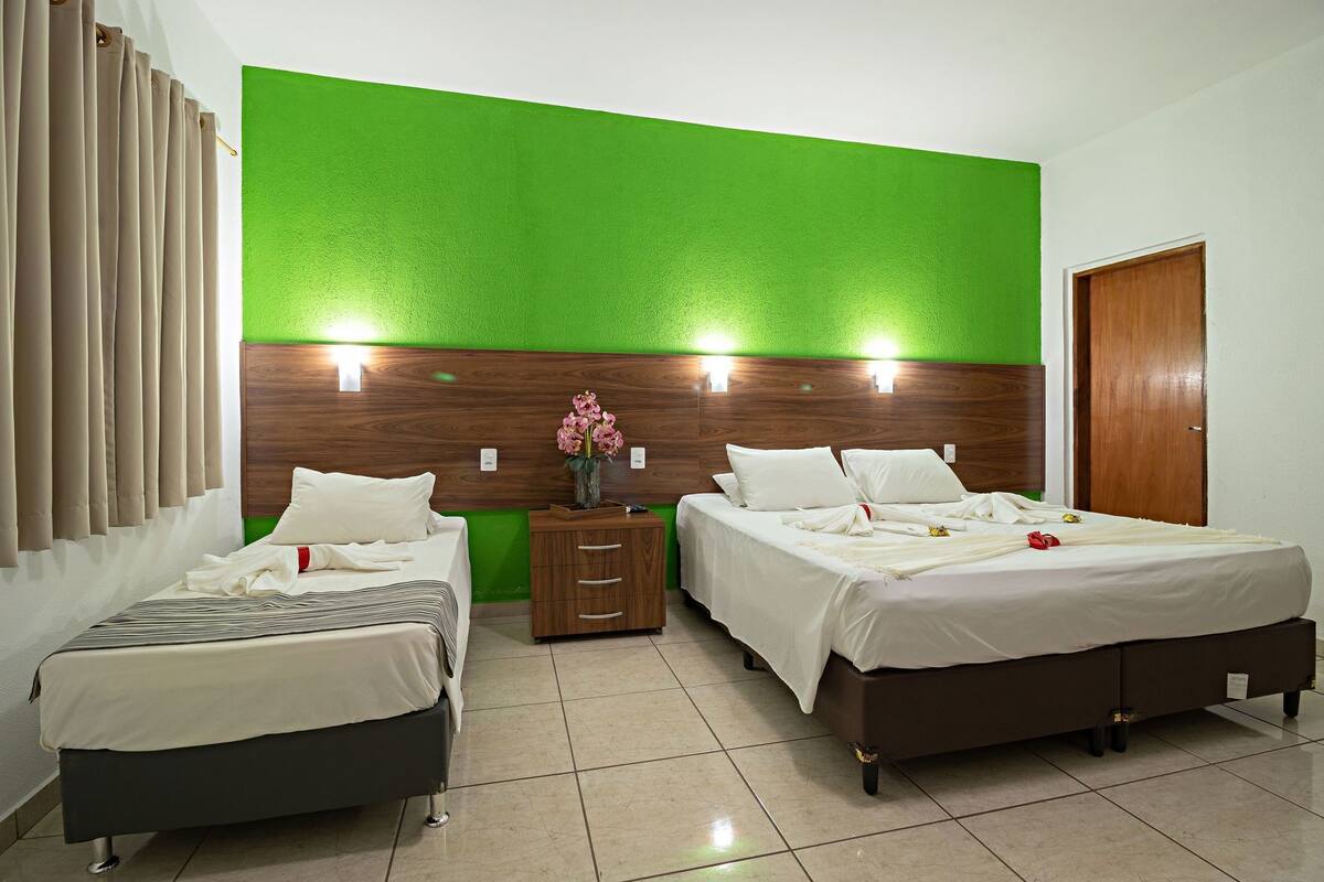 A hotel room with two beds, a wooden headboard, a green accent wall, and a wooden door.
