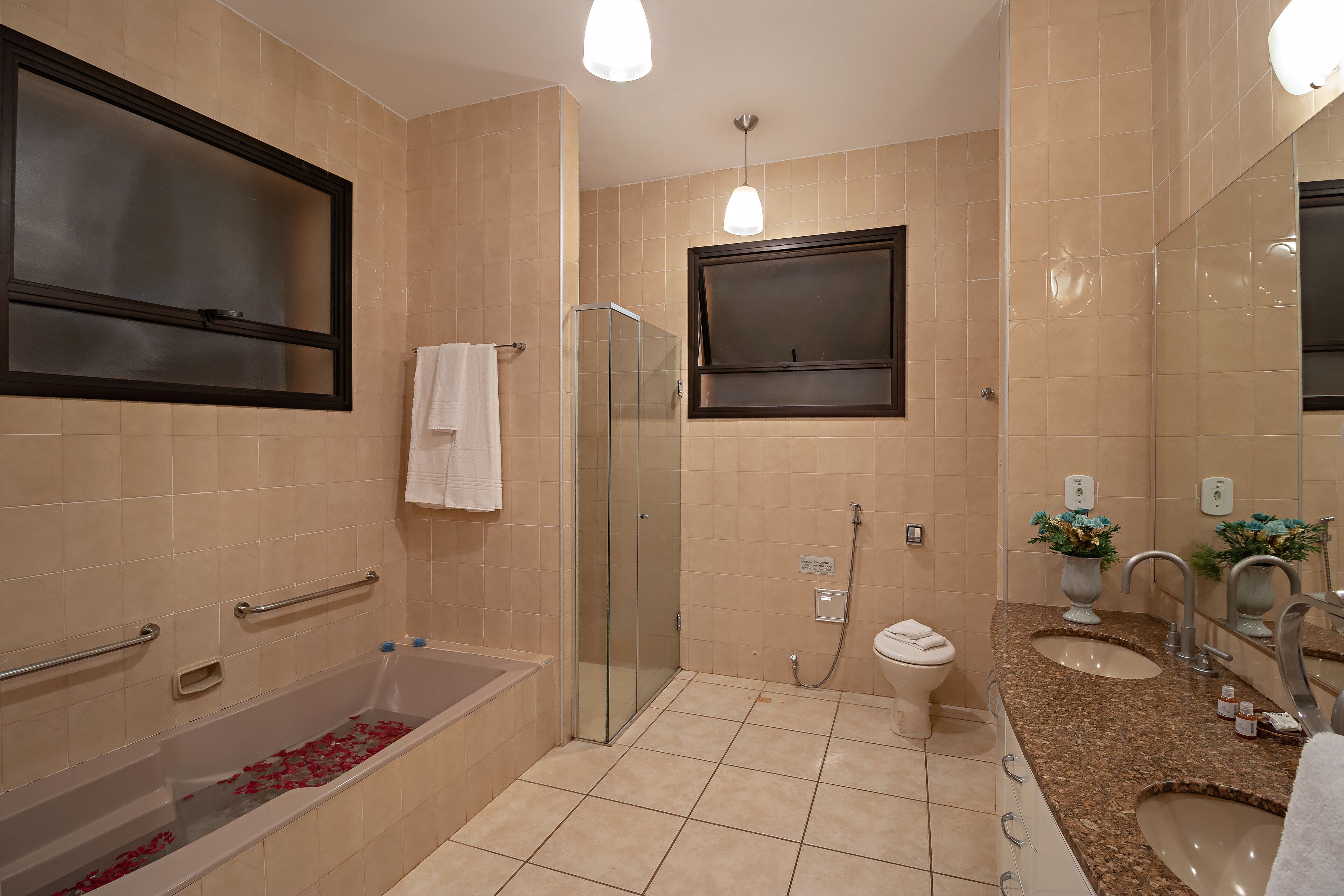 Un baño moderno con cabina de ducha de vidrio, una bañera con pétalos de rosa, un inodoro y un lavabo con tocador.