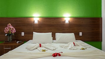 A neatly made bed with white linens and a red ribbon, a wooden nightstand with a vase of pink flowers, and a green wall with two wall-mounted lights.