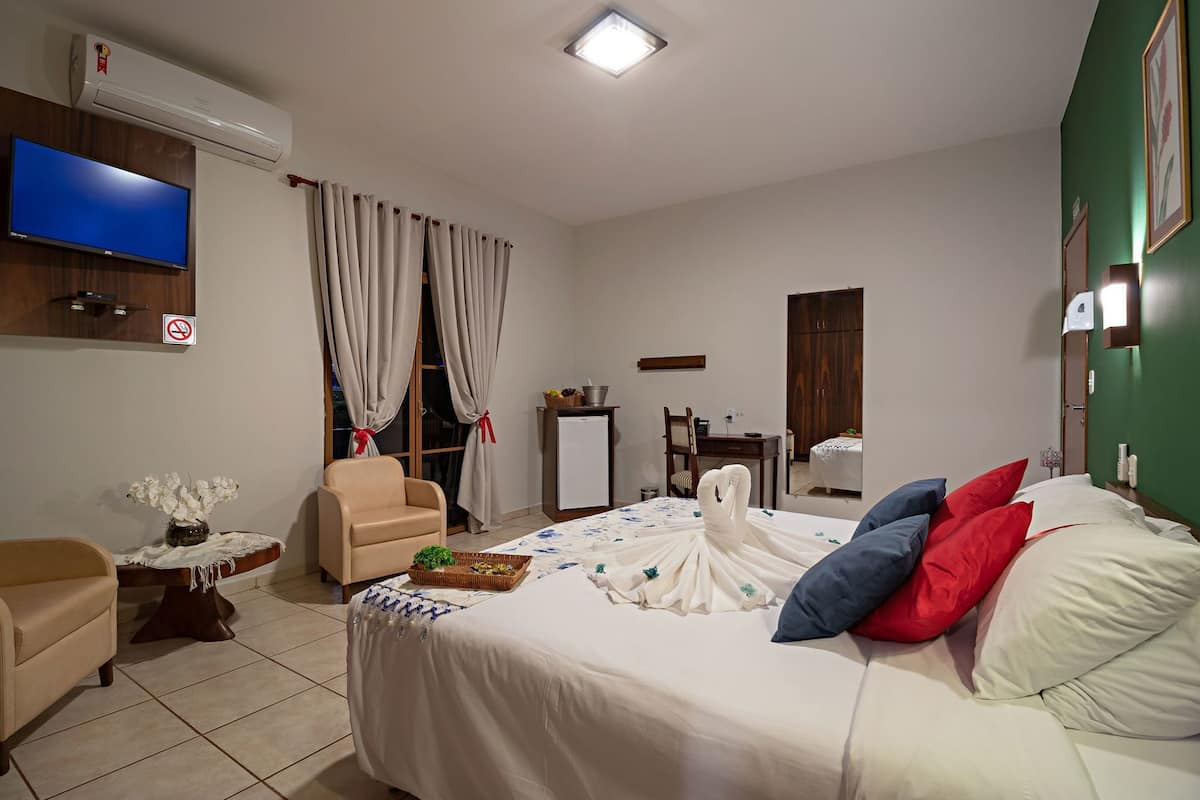 A hotel room with a bed, a TV, a desk, a chair, a dresser, and a bathroom door.