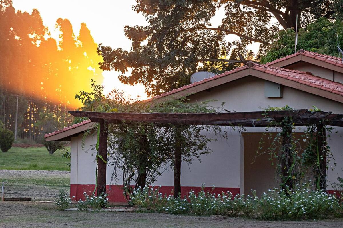 A building with a red roof and a white lower section, surrounded by greenery and flowering plants.
