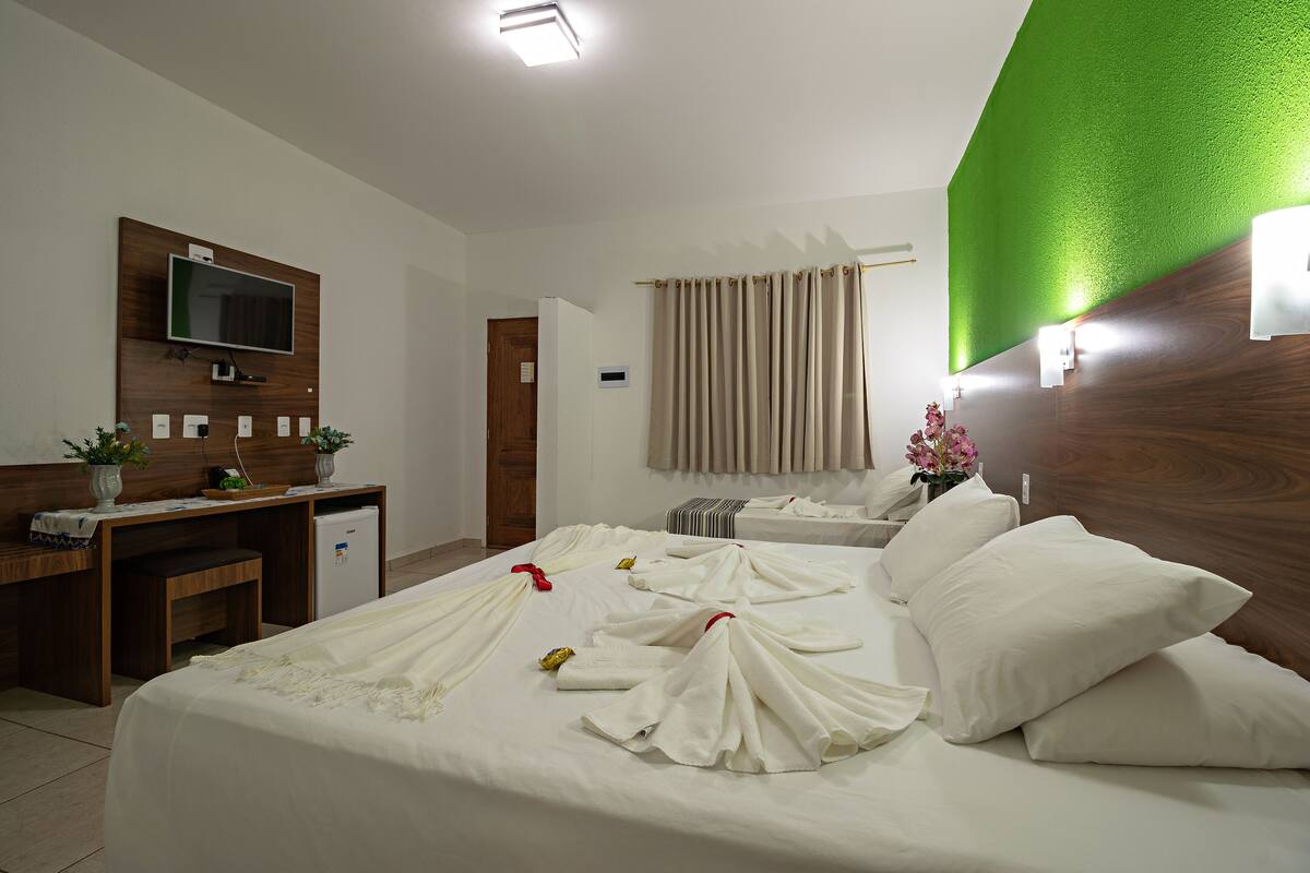 A hotel room with a bed, a desk, a television, and a green accent wall.