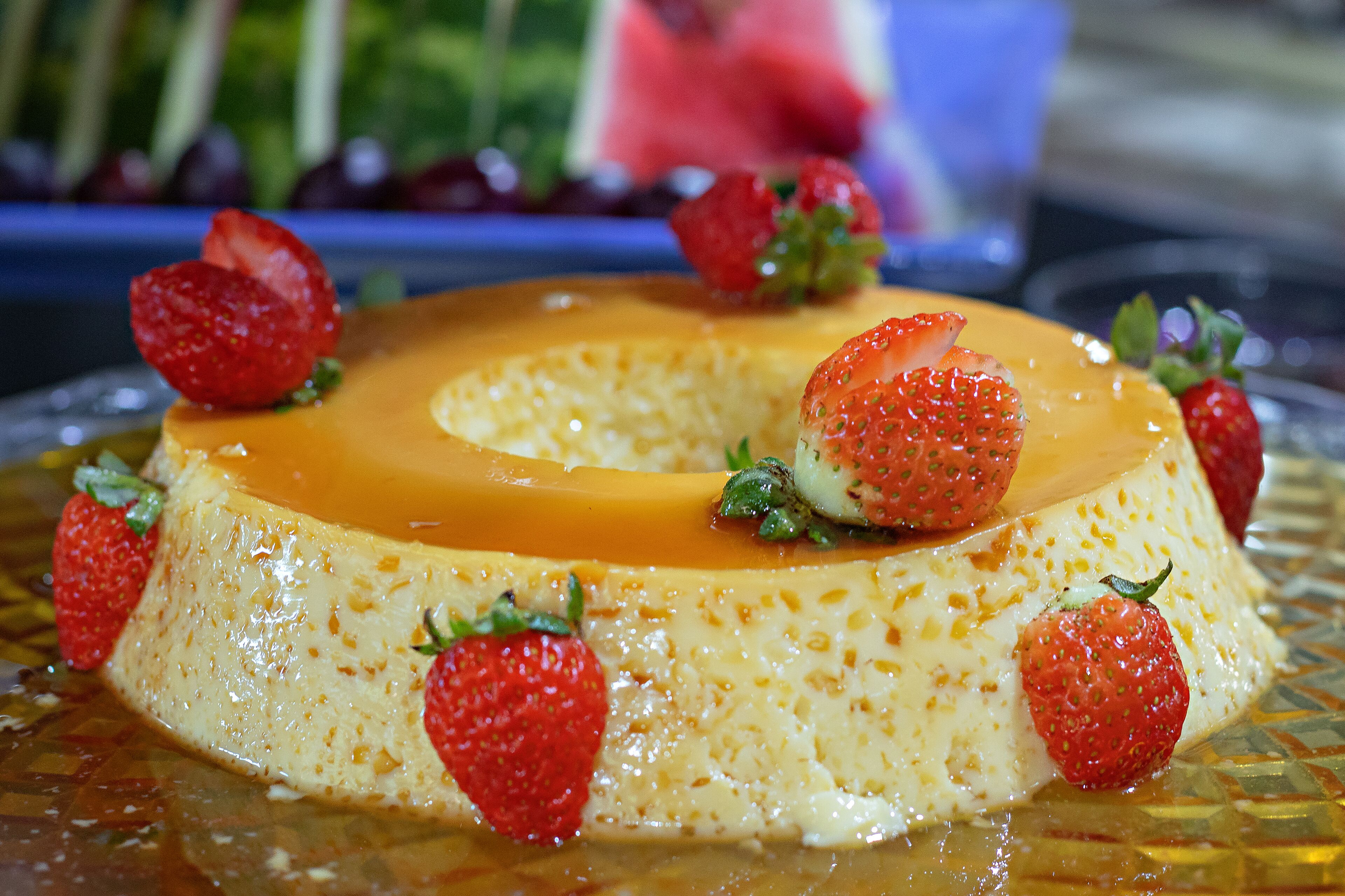 Un dessert composé d’une crème caramel et de fraises, présenté sur une assiette en verre.