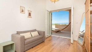 Una habitación con un sofá gris, suelo de madera y vistas a un balcón con una hamaca.