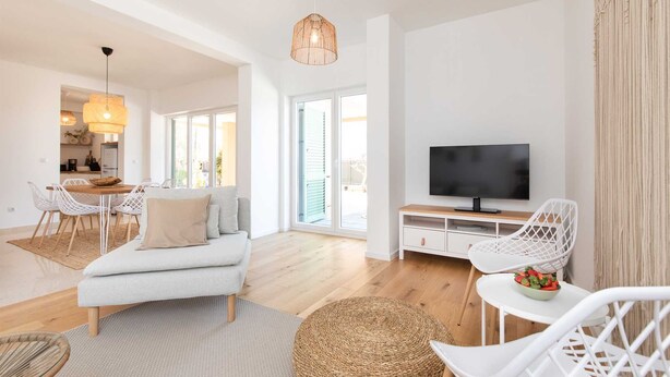 Una sala de estar moderna con sofá, comedor, televisor y mobiliario de mimbre.