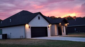 A single-story building with a gabled roof, a garage door, and a small porch area with lighting. - New Modern Home (Joplin)