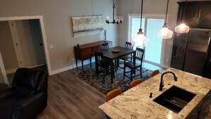 A modern kitchen with a marble countertop, a built-in sink, and a dining area with a table and chairs. - New Modern Home (Joplin)